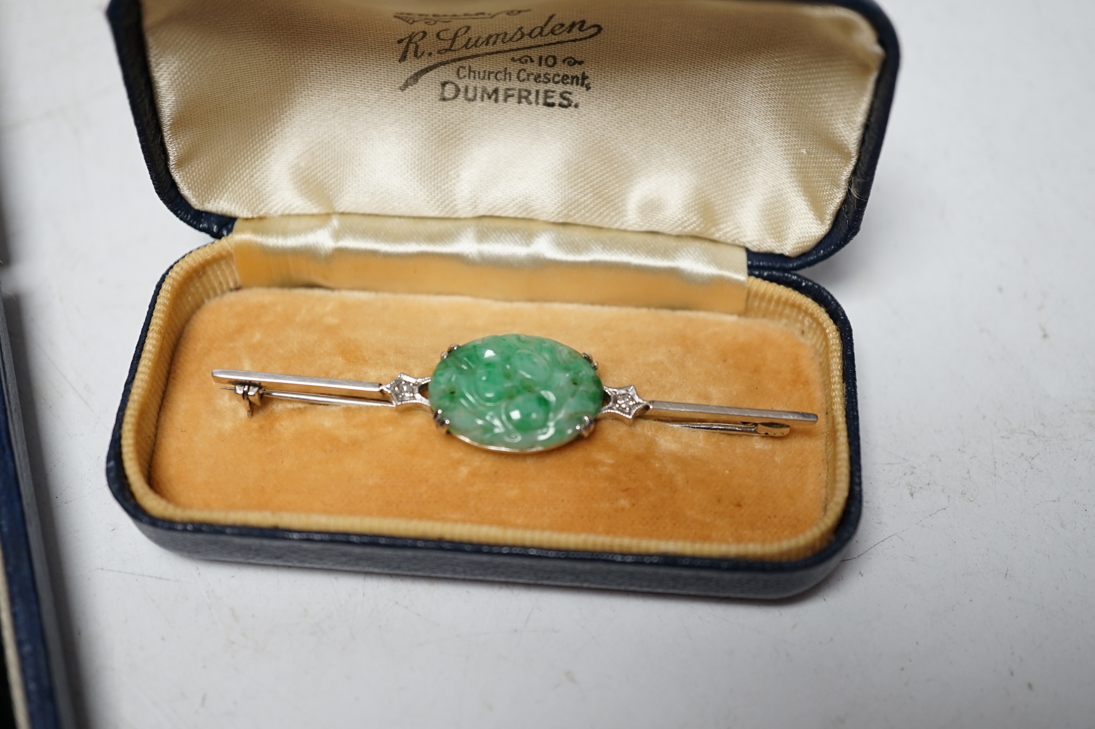 A cased 1930's white metal, single stone carved jade and two stone diamond set bar brooch, 62mm, a similar 9ct and carved jade set ring, a similar cased pair of 935 white metal, jade and marcasite set drop earrings and a